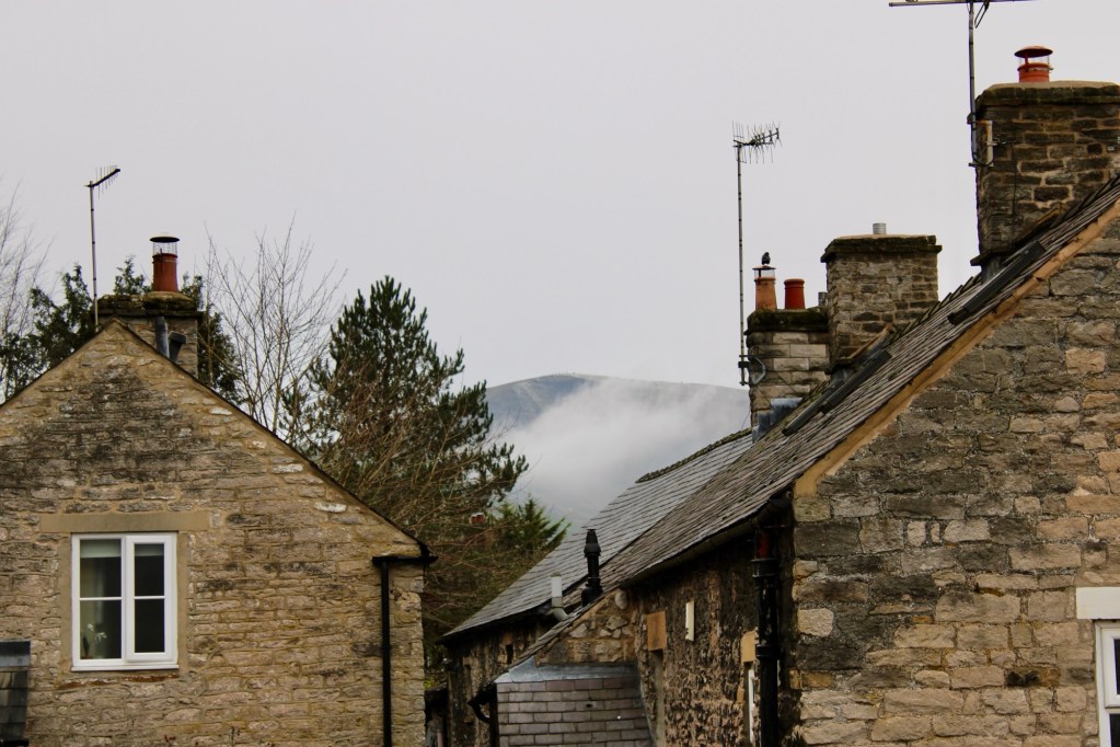 mam tor peaking through the clouds towering over the stone houses in castleton